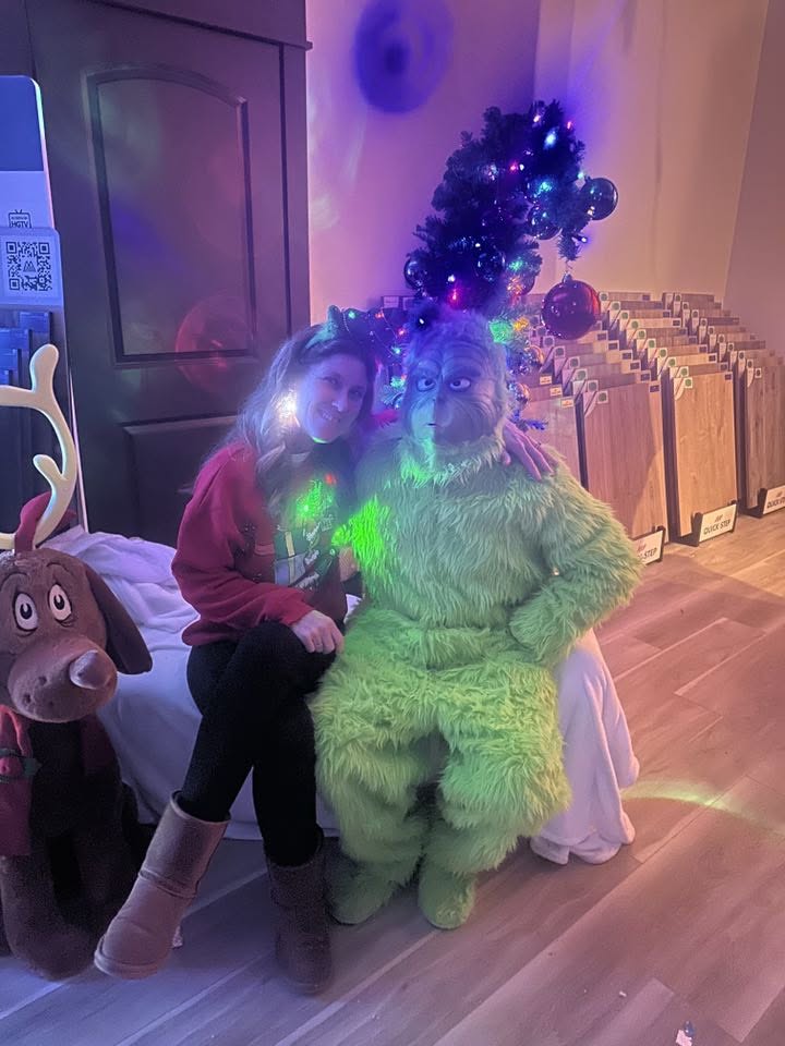Angela Johnson posing with a Grinch character in front of a decorated Christmas tree.