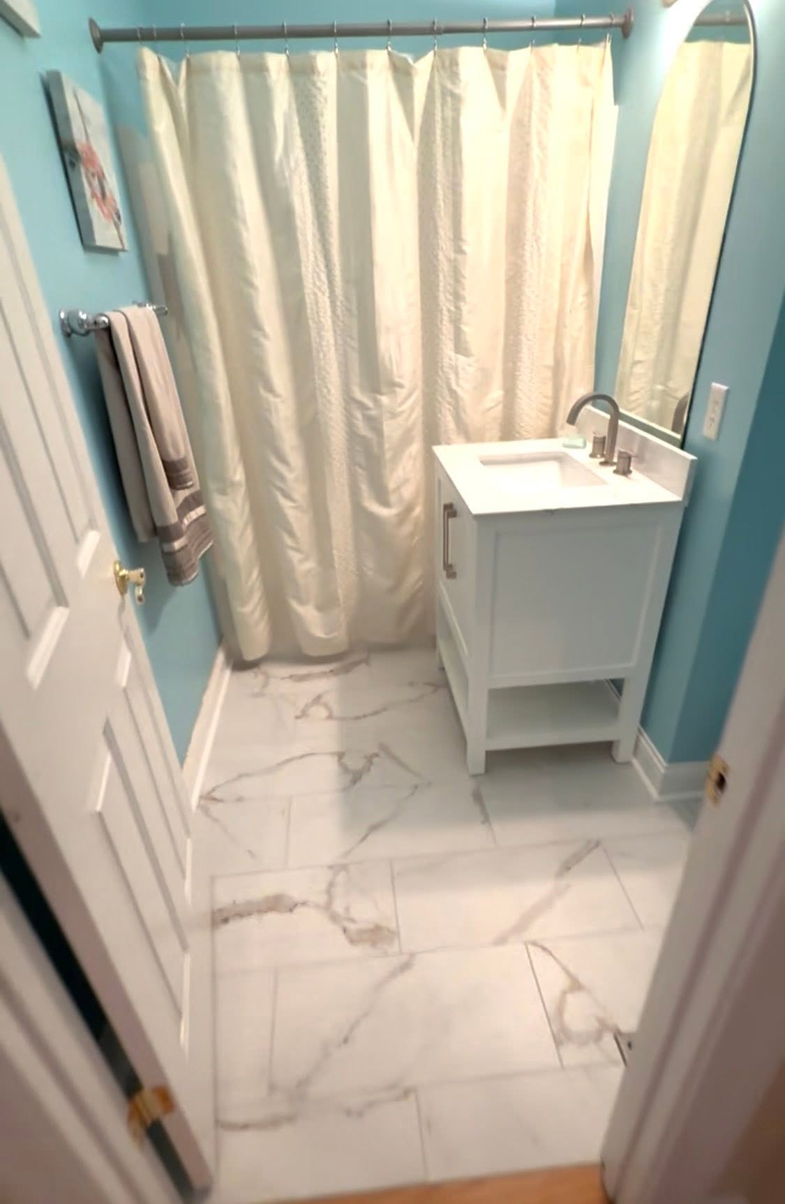 White marble-look tile flooring in a bathroom with teal walls.