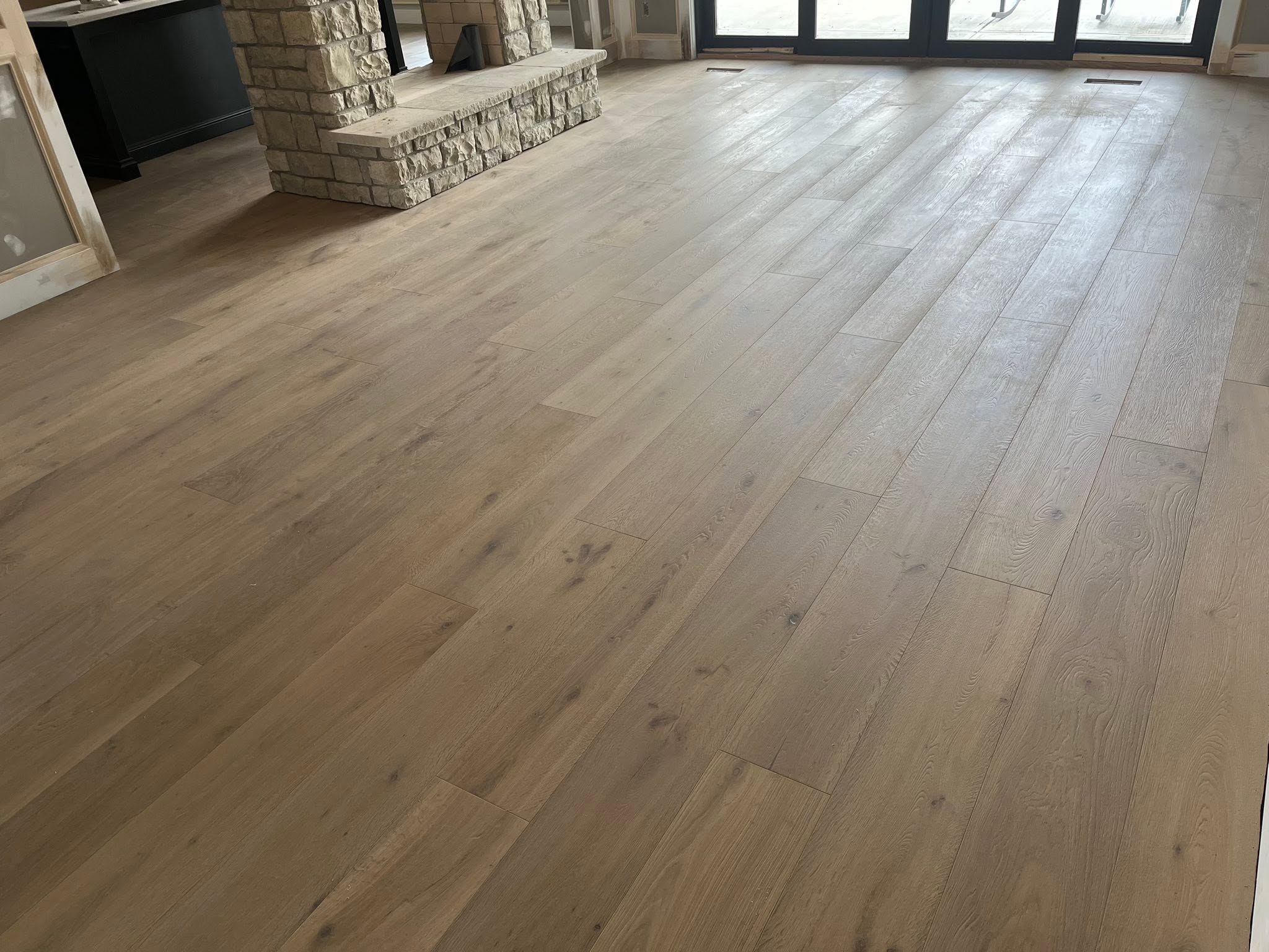 Whitewashed wide-plank hardwood flooring in a great room with a stone fireplace and sliding glass doors.