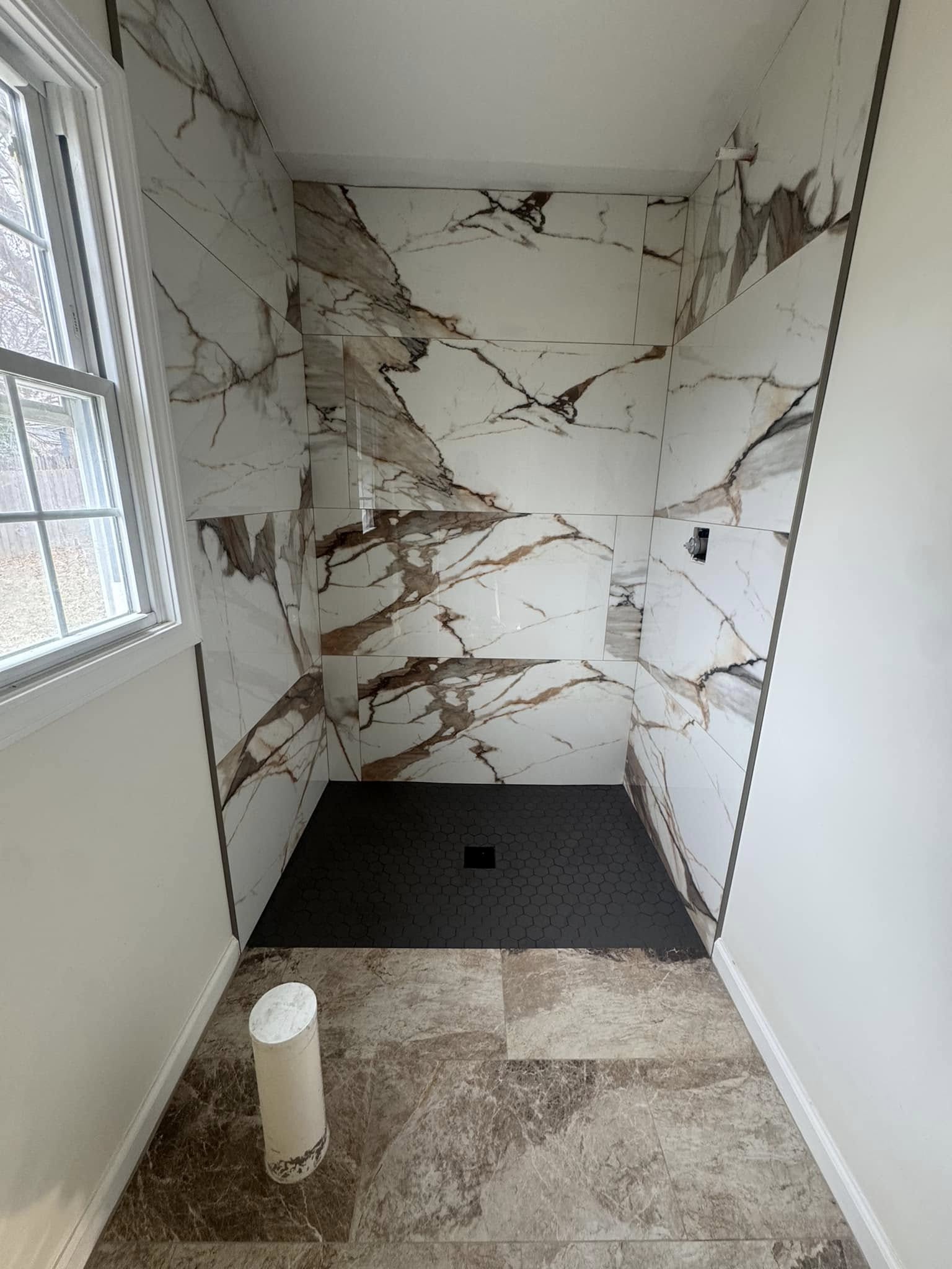 A marble-look tile shower with gold-brown veining and a black shower base.