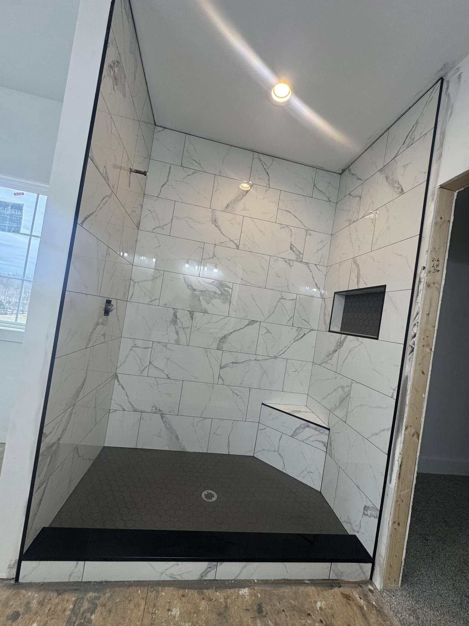 A white marble-look tile shower with a built-in corner bench and granite threshold.