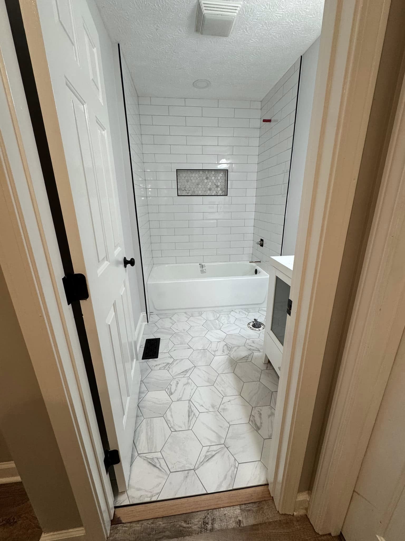 A white subway tile tub surround with a hexagon-tile niche and marble hexagon floor tile.