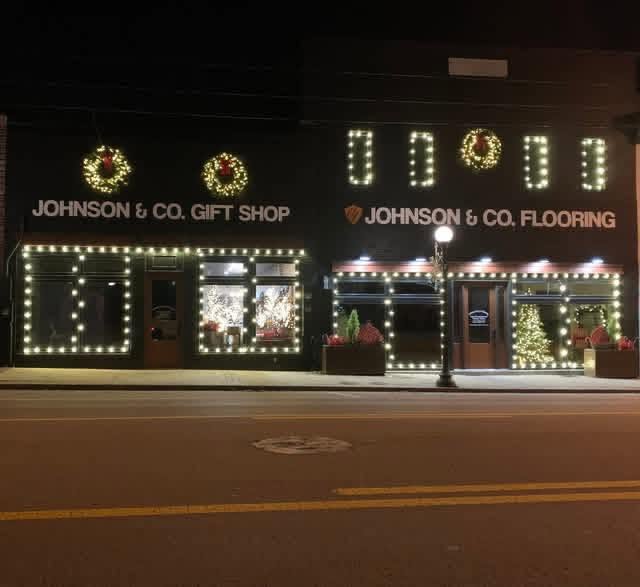 The Johnson & Co. Gift Shop and Flooring storefronts on Main Street in Eminence, lit up with Christmas lights and wreaths at night.