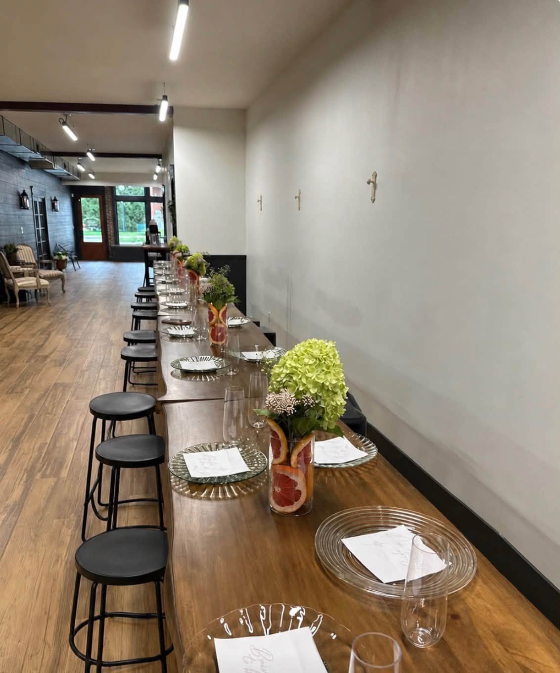 A long wood table set with glass plates, flutes, and hydrangea centerpieces along the wall at The Venue.